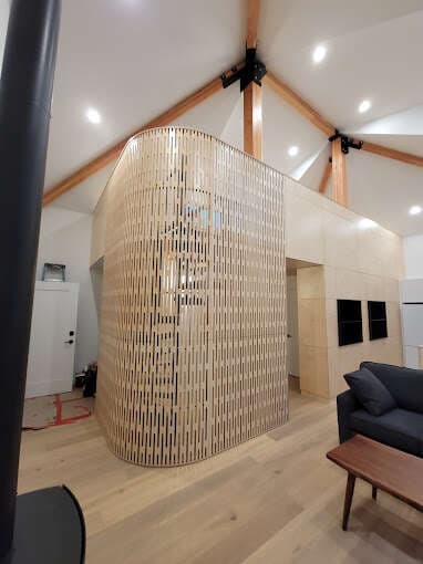 Curved vertical wood slat feature wall enclosing a nook beneath exposed timber trusses