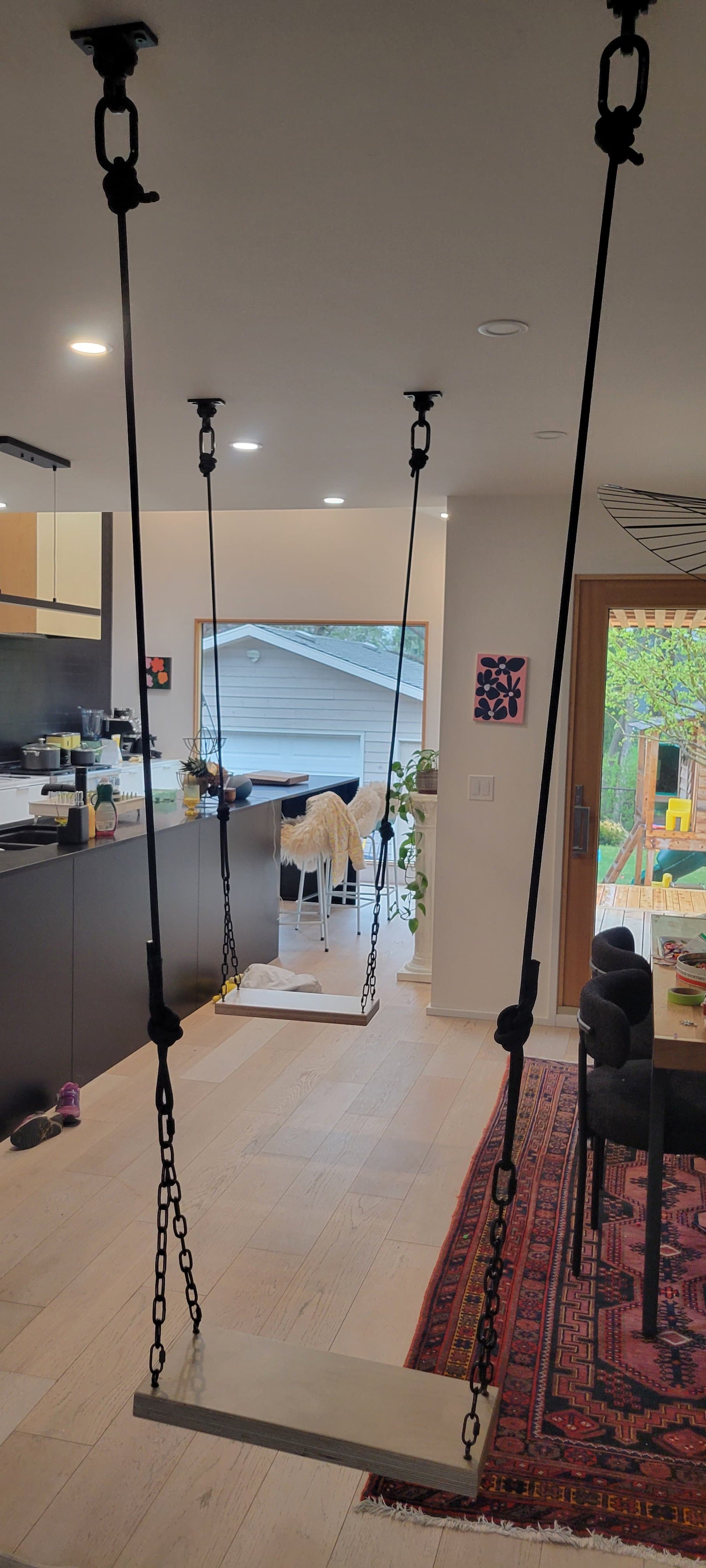 Two chain-hung bench swings suspended from the ceiling above an open kitchen and dining area