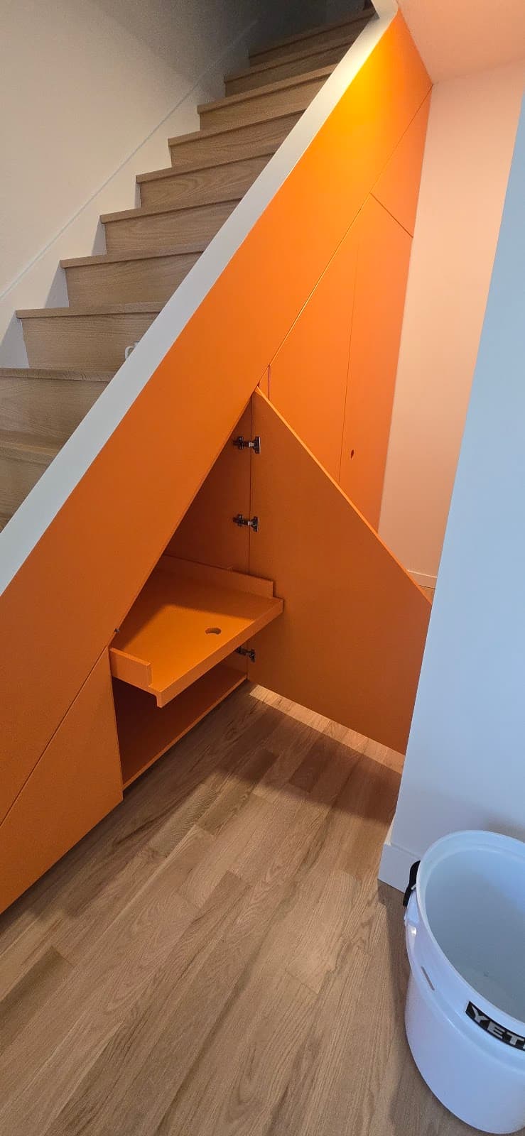 Bold orange custom under-stair storage cabinetry with an angled pull-out drawer